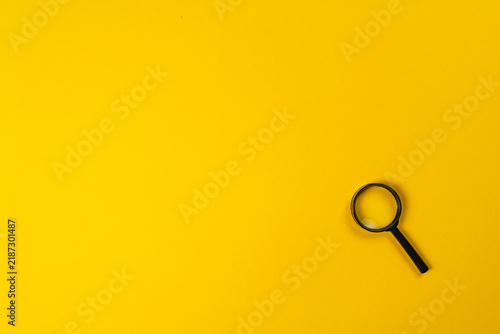 Magnifying glass on bright yellow background for examining details