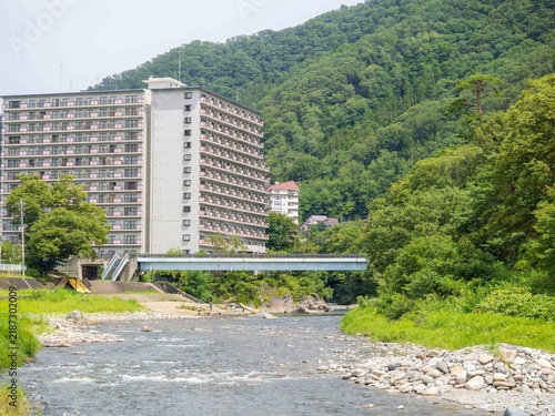Tapety artystyczne 緑豊かな山々と川のほとりに佇む大型ホテル