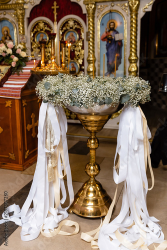 Foto Decorated baptismal font with white flowers and ribbons inside church