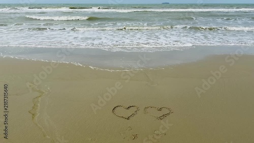Drawing heart shape on sandy shore by the ocean

