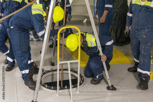 фотографія Seafarers working together during a shipboard rescue drill, assisting a crew member entering an enclosed tank to simulate the rescue of a person from a confined space