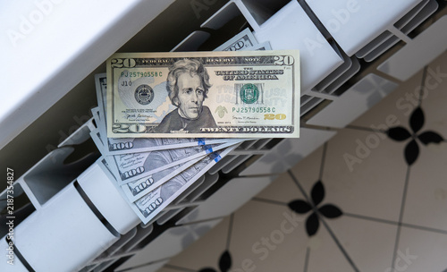 US dollar banknotes placed on a household radiator, illustrating heating costs, utility bills, taxes, inflation and financial pressure.