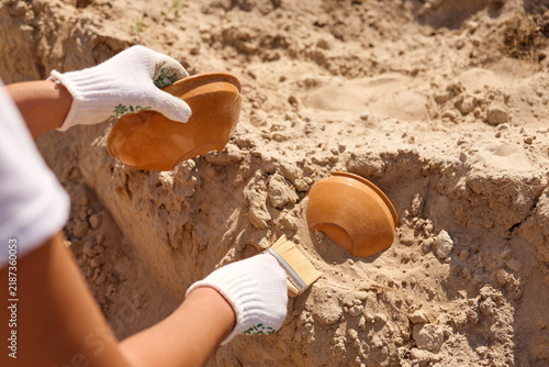 Fotografía Hands with gloves carefully brush sand away from two clay pots found during an e