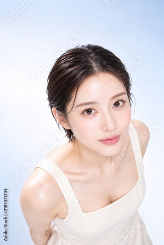 Naklejka 淡いブルー背景でカメラを見つめる若い日本人女性の透明感ある美容ポートレート