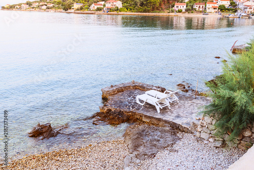 Cuadro en lienzo White sun loungers on stone platform by clear Adriatic water near coastal town