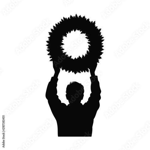 Man silhouette raising a big green pine branch wreath high above his head with both hands