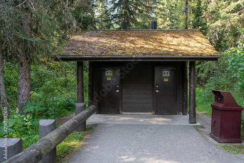 Forest restroom with wooden doors and shingled roof