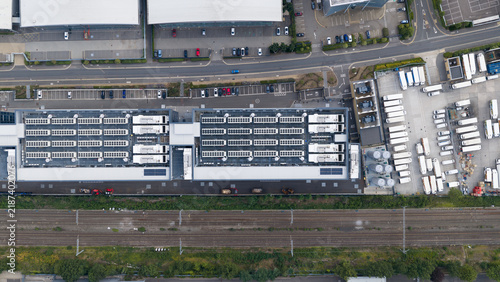 Aerial view of a large industrial facility featuring numerous rooftop HVAC units, a parking lot with vehicles, and adjacent railway tracks in Slough, England, United Kingdom.