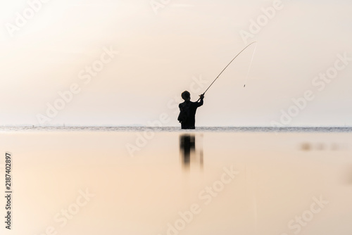 Pescador en la playa un amanecer con barco de fondo y el mar en calma
