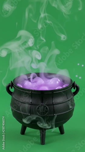 Black Cast Iron Witch Cauldron Bubbling with Purple Potion and Smoke - An antique-style black cast iron cauldron sits on a green background, bubbling with a mystical purple potion.
