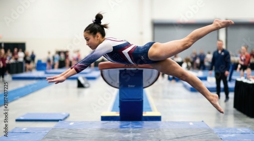 Young female gymnast performs vault in competitive gymnastics event.