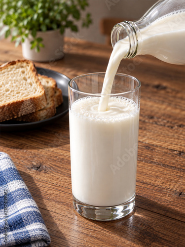 Pouring Fresh Milk from Bottle into Glass on Wooden Table.