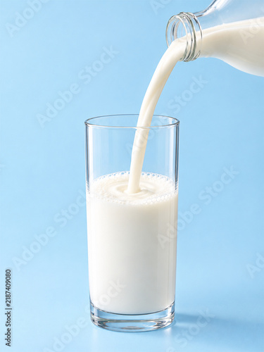 Pouring Fresh Milk from Glass Bottle into Glass on Light Blue Background.
