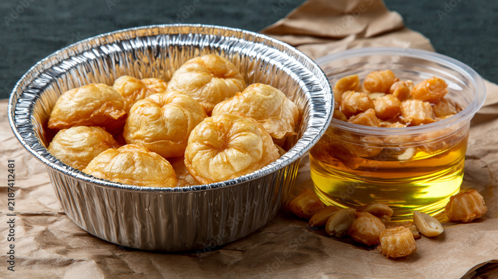 Obraz premium Small fried corn puff snacks in a metal bowl beside a clear cup of golden cooking oil