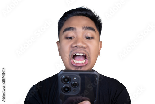 Принти на полотні Shocked and startled Indonesian man in a black t-shirt looking down at his smartphone with a wide open mouth and bulging eyes against a white background