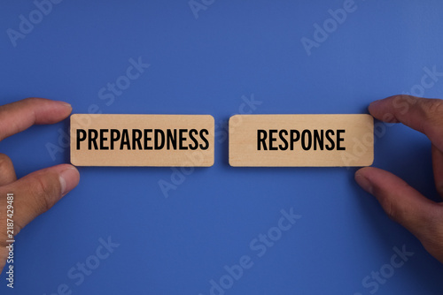 Wooden blocks labeled preparedness and response held by hands on a blue background, representing emergency planning, readiness, crisis management, and disaster response.
