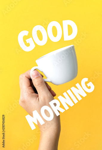 Cheerful good morning greeting with a hand holding a white coffee cup on yellow background