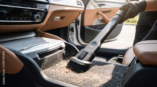Detailer Vacuuming Dust and Dirt from Modern Car Dashboard Interior