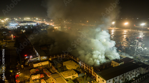 Aerial view of a large fire burning at an airport facility at night, with thick smoke rising into the air and emergency vehicles responding on the ground in Dhaka, Dhaka Division, Bangladesh.