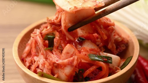 Close-up of chopsticks picking up Kimchi Napa cabbage from a wooden bowl, Korean side dish (Banchan), slow motion shot