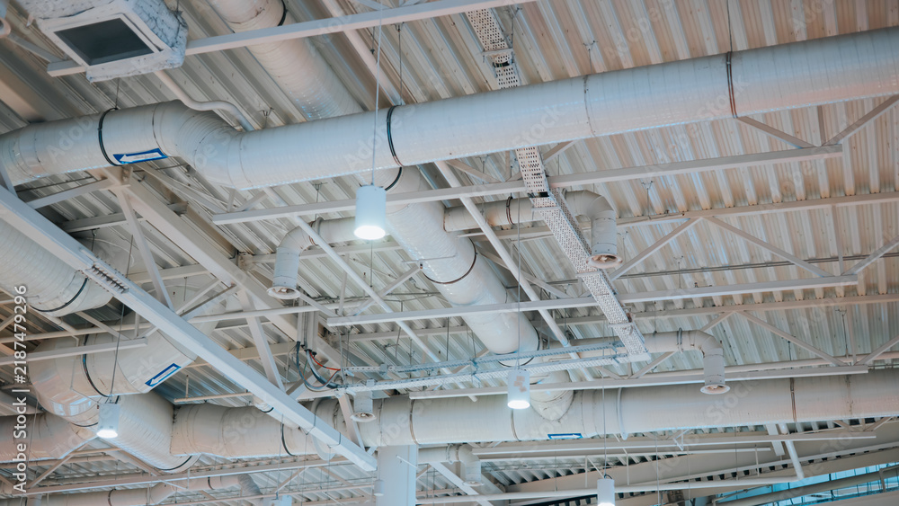 Obraz premium The ceiling features multiple ventilation ducts and lights arranged in a grid pattern. The setting appears to be an indoor commercial space with a focus on functionality