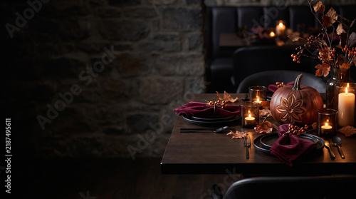 Carved pumpkin centerpiece with glowing candles and deep burgundy napkins arranged on a rustic wooden table for festive dinner