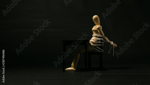 Obraz na plátně Wooden mannequin tied to a chair with rope in dark room, hostage concept