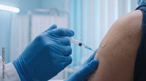Doctor in blue medical gloves administering a vaccine injection into a patient arm in clinic with healthcare professional uses syringe administer injection arm patient clinical setting immunization