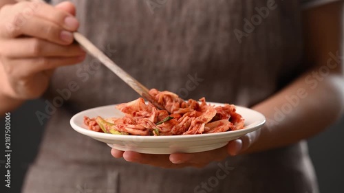 Woman hand holding a plate of Kimchi Napa cabbage and using chopsticks to eat, Korean side dish (Banchan)