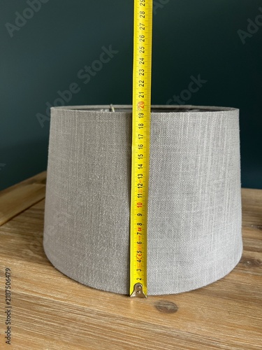 Fotografía A fabric lampshade stands on a table while being measured with a ruler, highlighting the importance of choosing the right size for a wall sconce