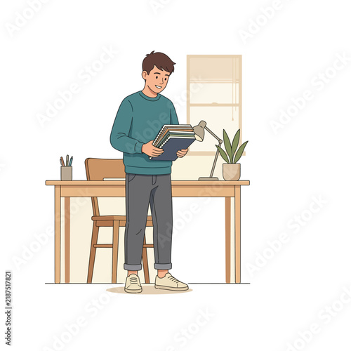 Young man diligently holding a stack of educational books while standing by a study desk in a cozy home office setting, preparing for learning and personal development