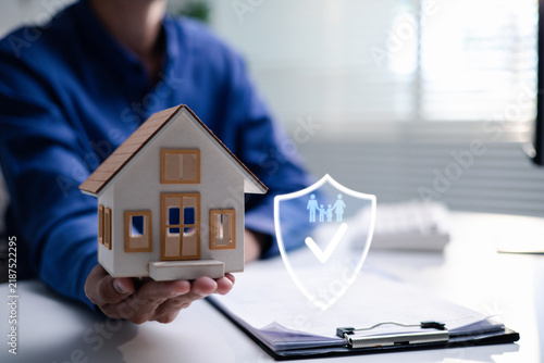 Fotografie Insurance professional presents a model house beside policy documents