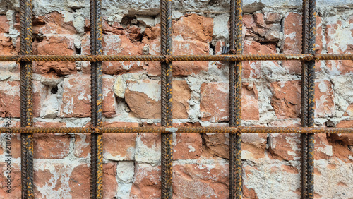 Canvastavla A grid of rusted rebar reinforcement bars installed in front of an old, weathered red brick wall with peeling mortar and concrete patches