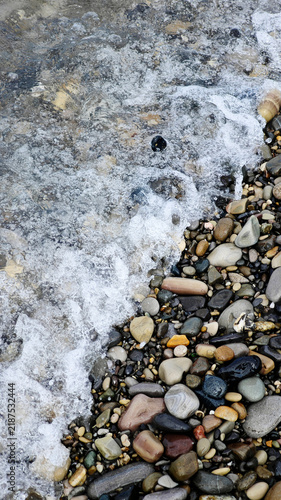 Obraz na plátně A close-up view of pebbles on a beach with gentle waves lapping at the shore