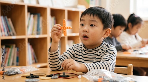 Young Asian Boy Holding Toy Gear During STEM Education Class In Library