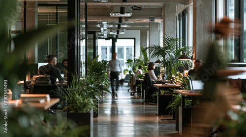 A busy open-plan modern office with employees working at desks surrounded by green plants. Ideal for workplace productivity and biophilic design themes.