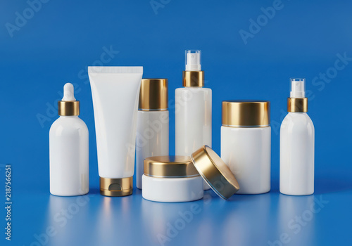 Set of white cosmetic bottles with golden caps on a blue surface
