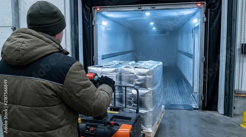 Professional warehouse worker operating electric pallet jack to load temperature-sensitive pharmaceutical cargo into refrigerated trailer, ensuring smart cold chain logistics efficiency.
