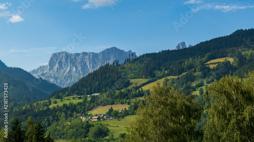 Panoramic View from a Mountain Peak Across the Green Alpine Forests, Snow-Capped Mountains, and Scenic Valleys of Switzerland Under a Cloudy Summer Sky