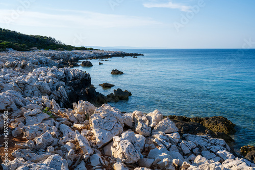 Fotografie The rocky Mediterranean coast of the island of Cres, featuring blue sea waves, dramatic cliffs, a natural stony shore, and a summer seaside landscape