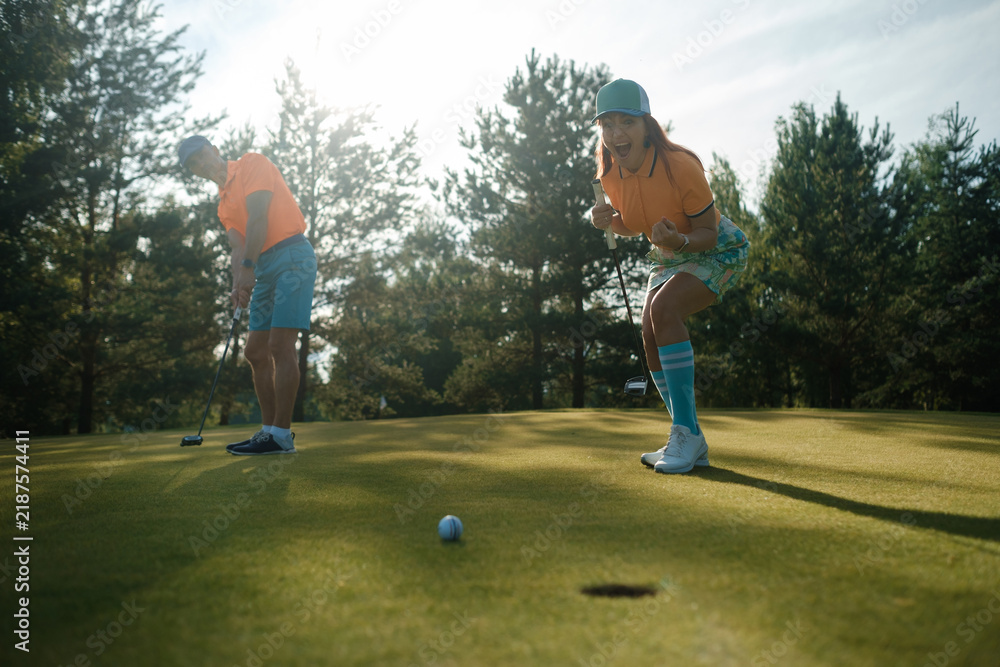 Obraz premium Golfers enjoying a sunny afternoon on a beautifully manicured course, celebrating a successful putt while surrounded by lush trees and greenery