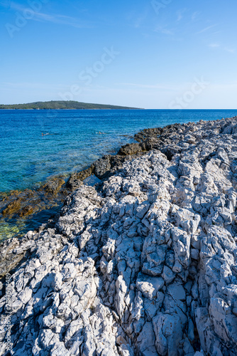 The rocky Mediterranean coast of the island of Cres, featuring blue sea waves, dramatic cliffs, a natural stony shore, and a summer seaside landscape.