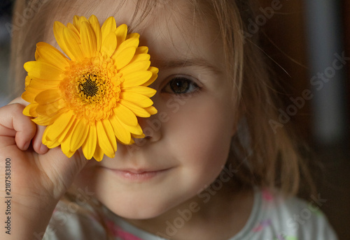 Young girl with a bright yellow gerbera flower beside her face, close-up portrait of a child, natural beauty, innocence and childhood concept.