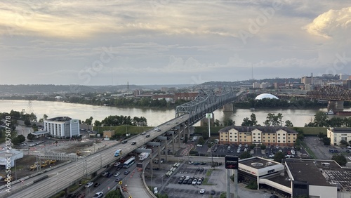 Covington, United States - 18 July 2026: Aerial view of the Ohio River with the Brent Spence Bridge carrying traffic, surrounded by urban infrastructure and buildings under a cloudy sky.