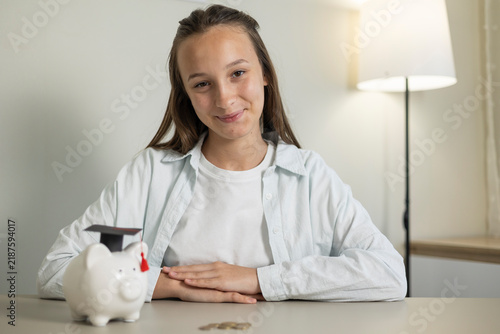 Canvastavla Teenage girl saving money in a piggy bank, holding a coin and learning about per