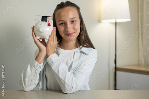 Canvastavla Teenage girl saving money in a piggy bank, holding a coin and learning about per