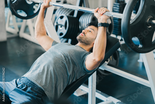 Obraz na plátně Focused man doing gym fitness exercising health care with barbell bench press fo