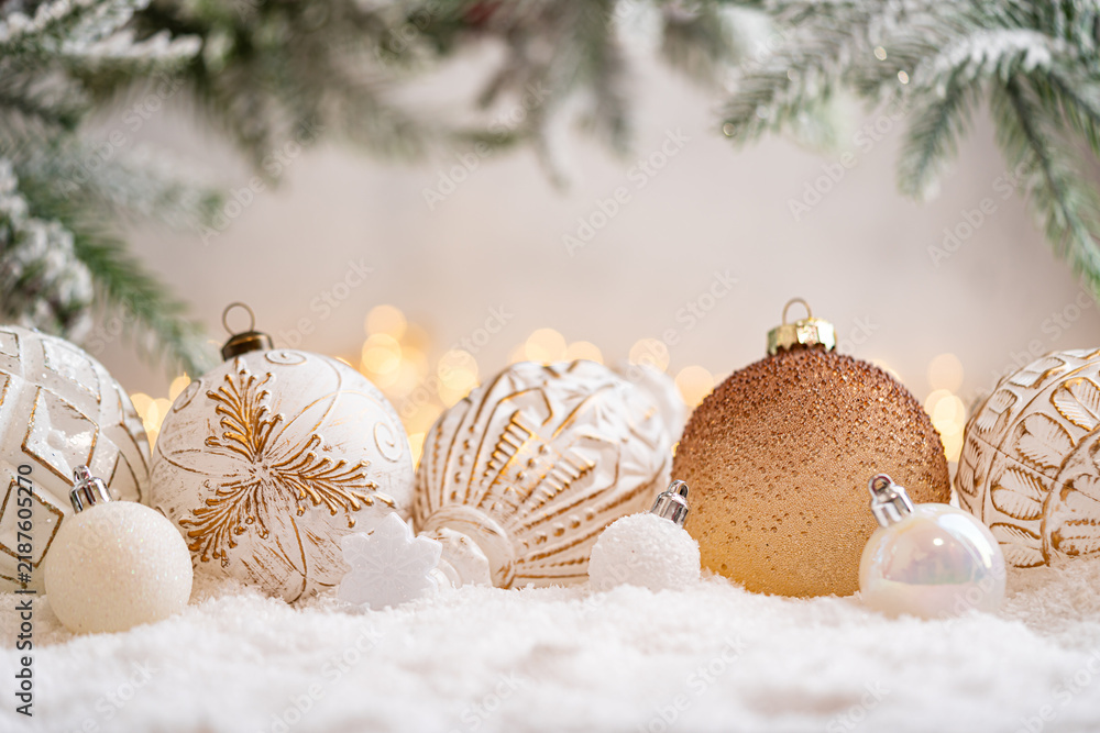 Naklejka premium A Christmas background featuring a row of textured white and gold baubles with etched patterns beside a bronze glitter ornament beneath frosted pine on snow, softly lit by warm twinkling lights.