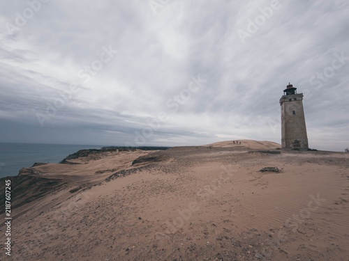 Fotografie Rubjerg Knude Lighthouse standing in shifting sand dunes under dark stormy sky,