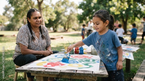 Indigenous woman watches young child paint outdoors during art class